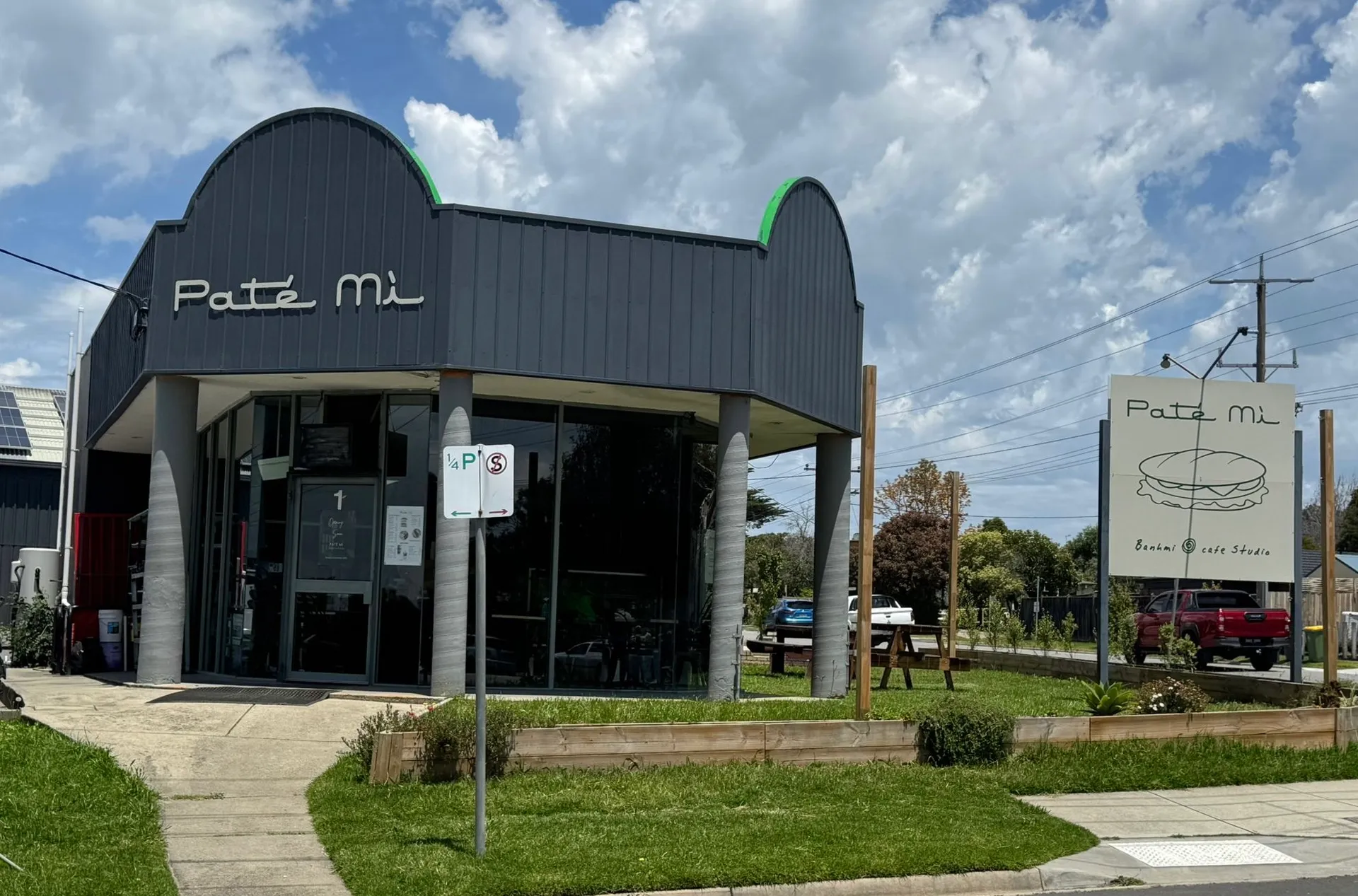 Pate Mi cafe exterior with charcoal barrel-vault roof, signage and kerbside banh mi sign under blue sky