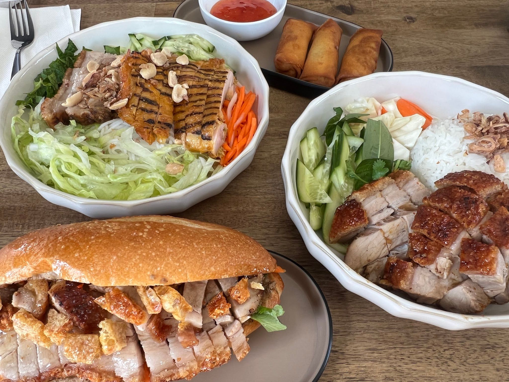 Spread of Vietnamese dishes: crispy pork banh mi, noodle salad bowls, spring rolls and dipping sauce