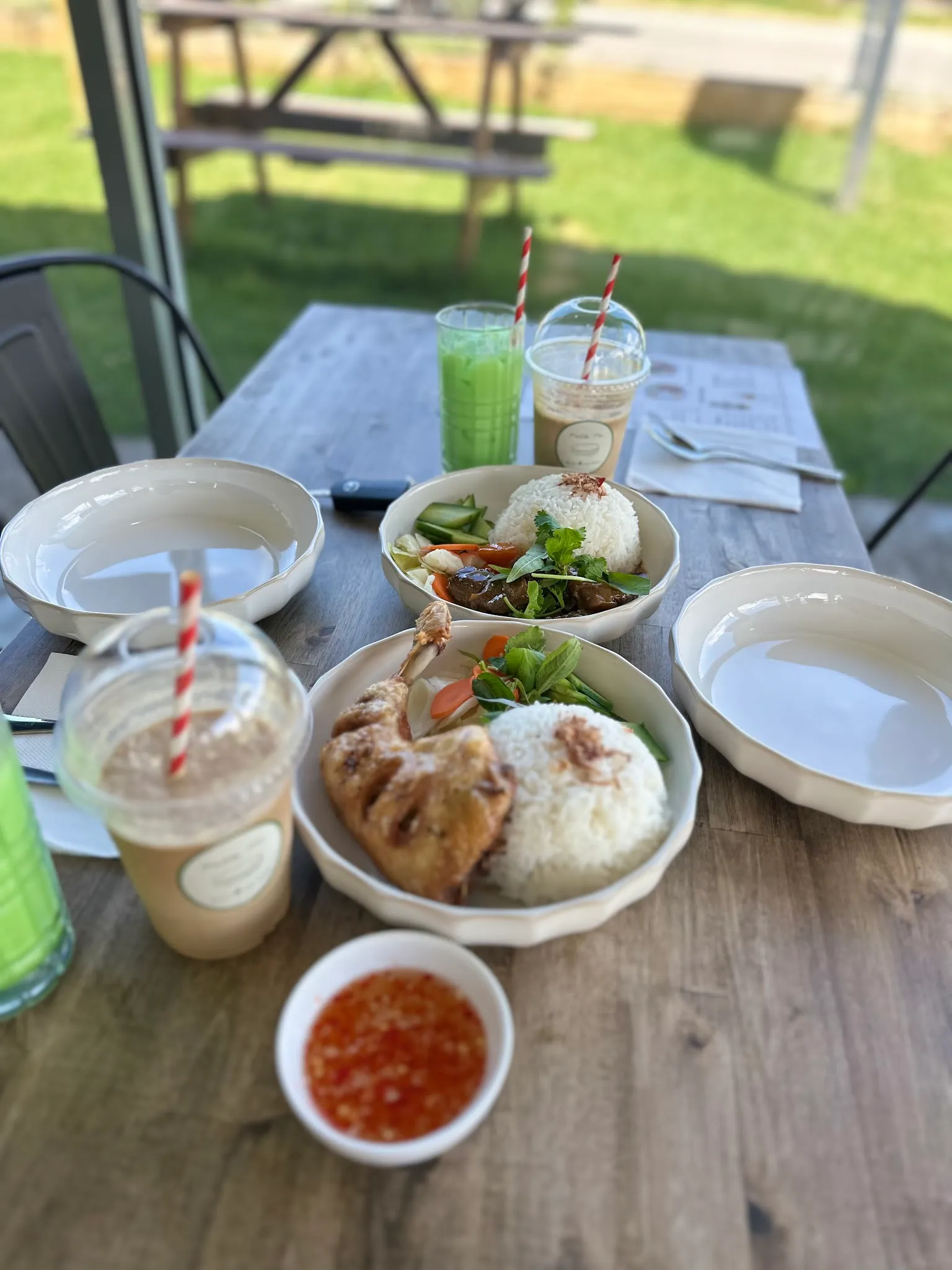 Rice plates and Vietnamese drinks on a window table with green lawn and picnic bench outside
