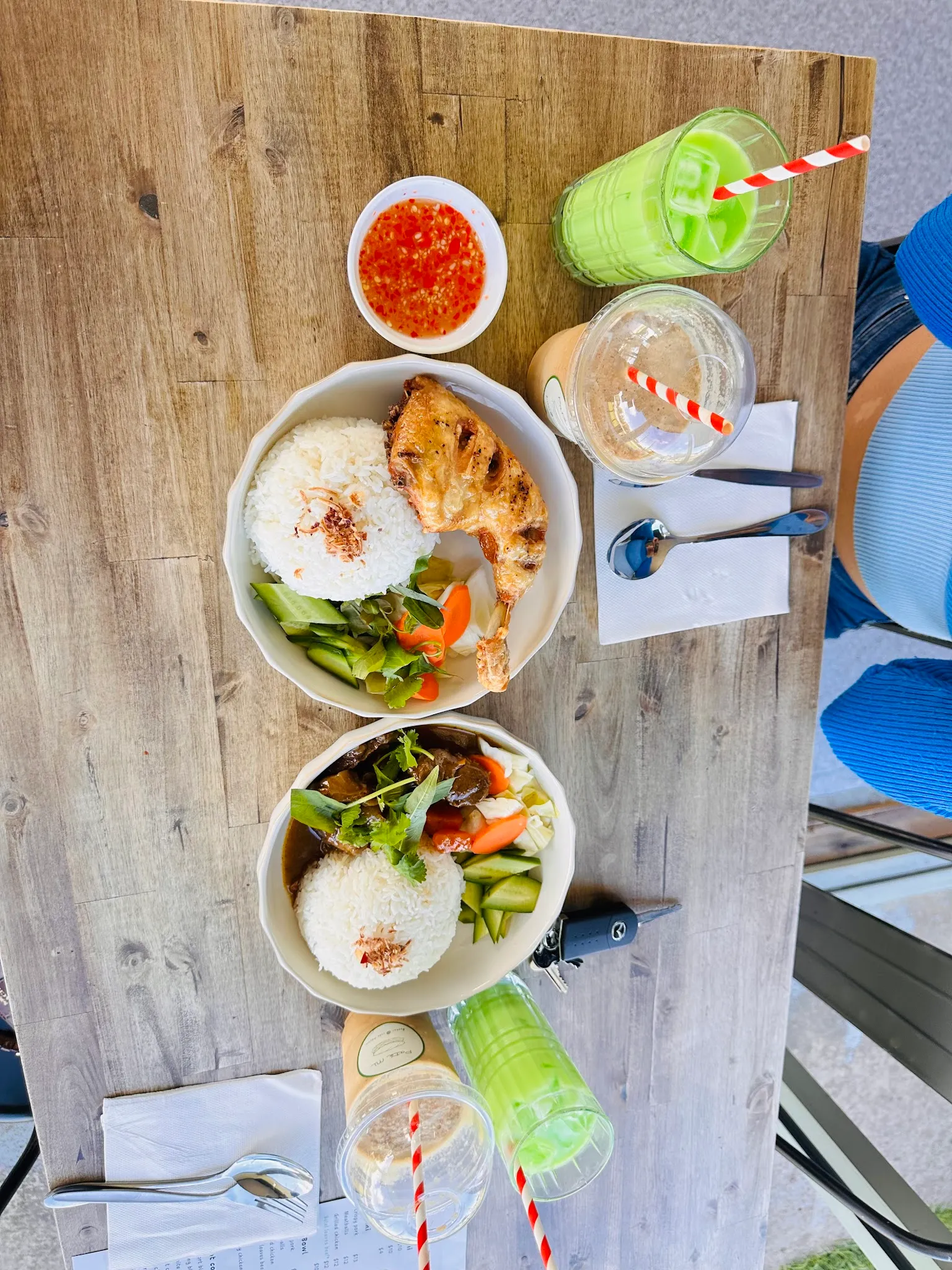 Overhead flat-lay of two rice meals with green and iced coffee drinks on a wood table
