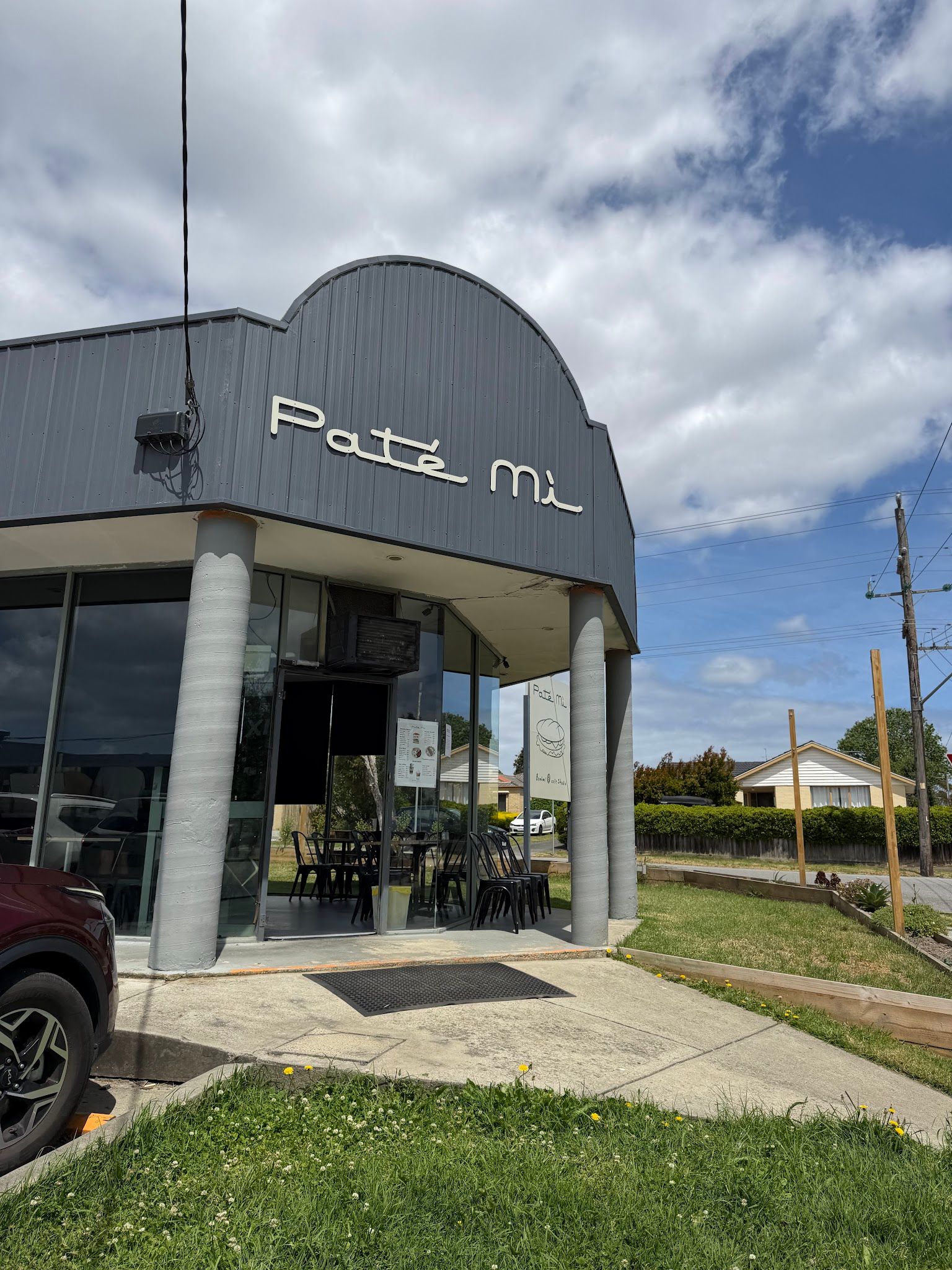 Close exterior of Pate Mi shopfront with signage and curved charcoal roof on a cloudy day
