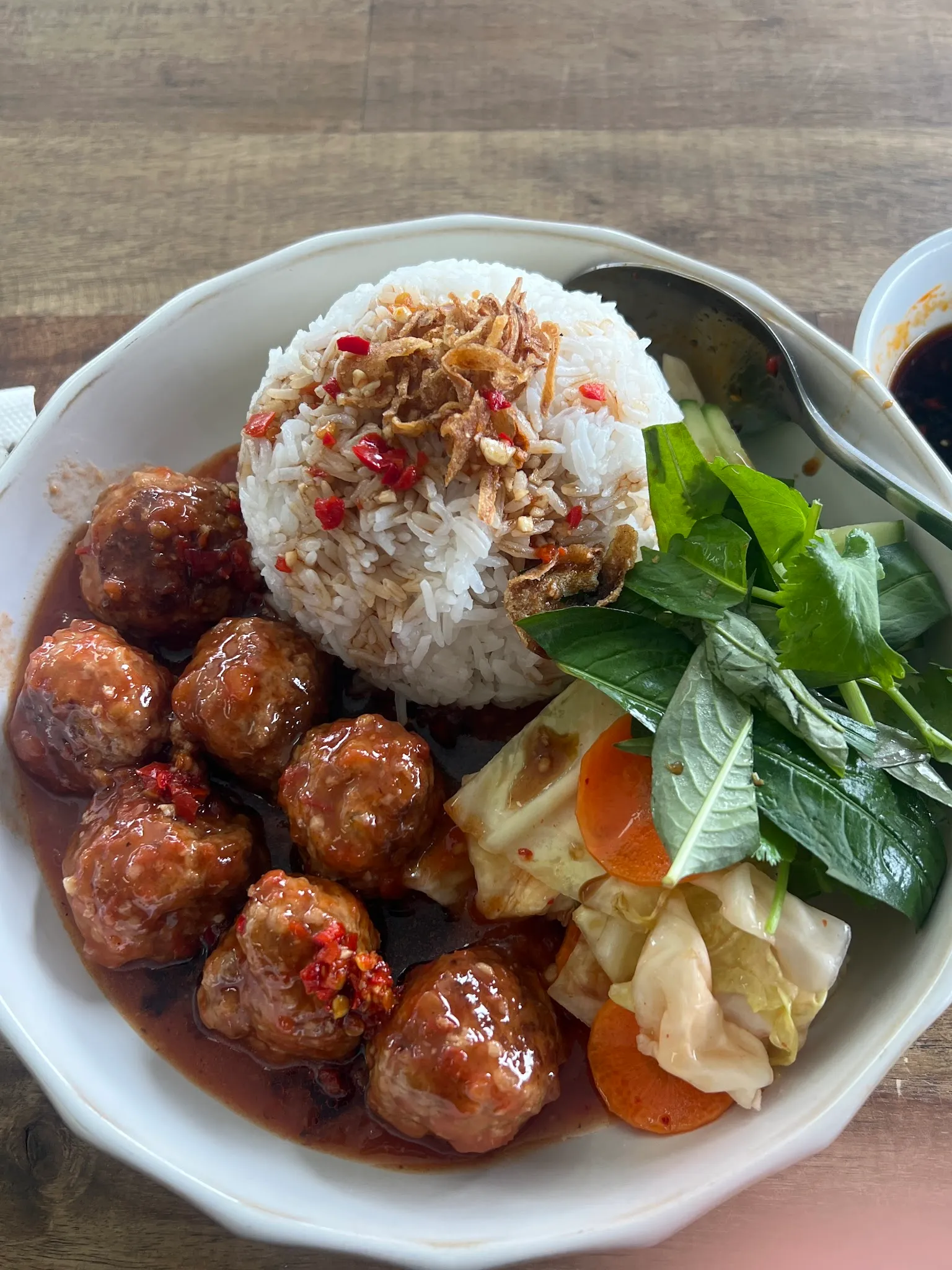 Bowl of glossy chilli-glazed Vietnamese meatballs over rice with herbs and pickled vegetables