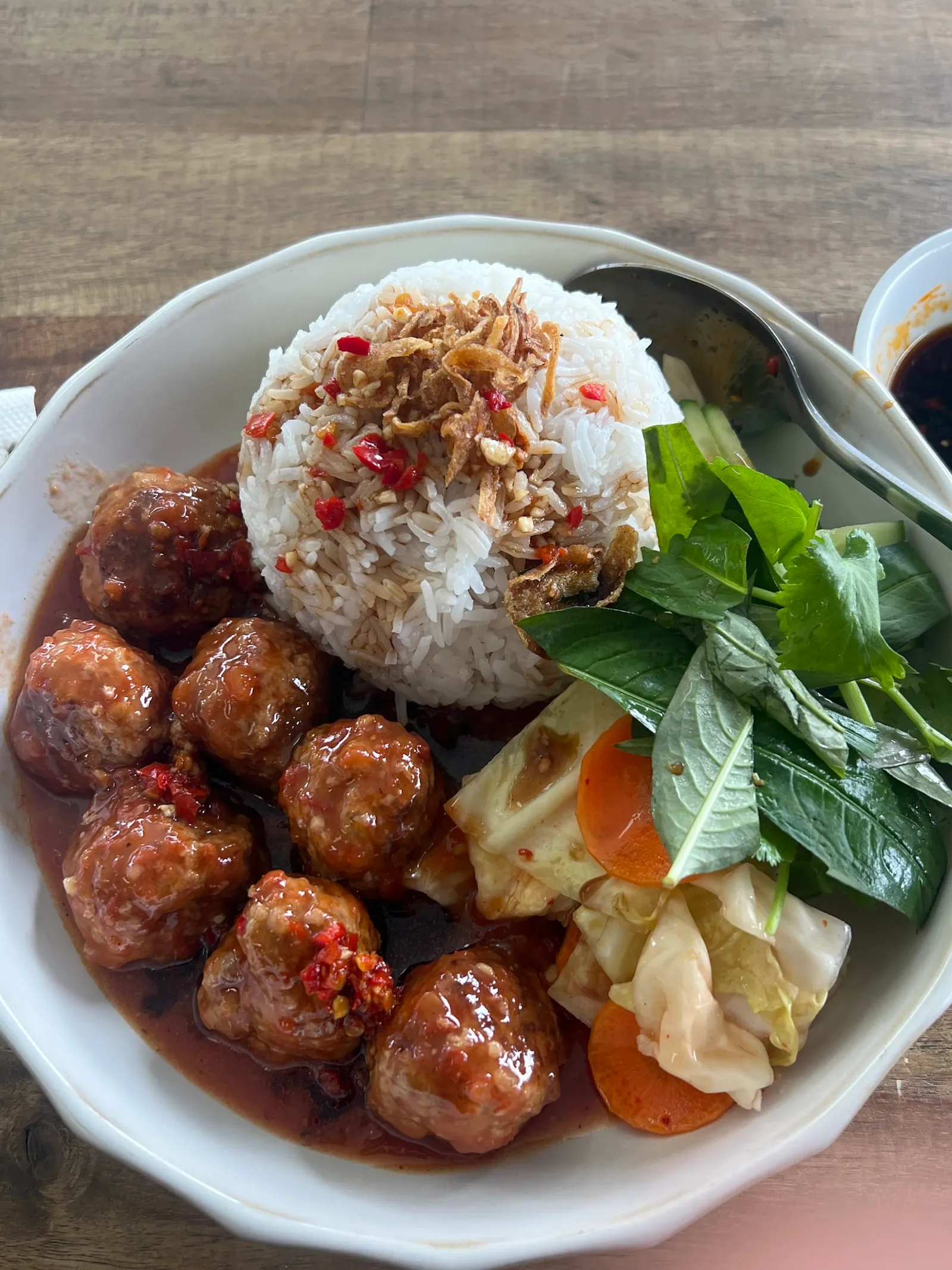 Bowl of glossy chilli-glazed Vietnamese meatballs over rice with herbs and pickled vegetables