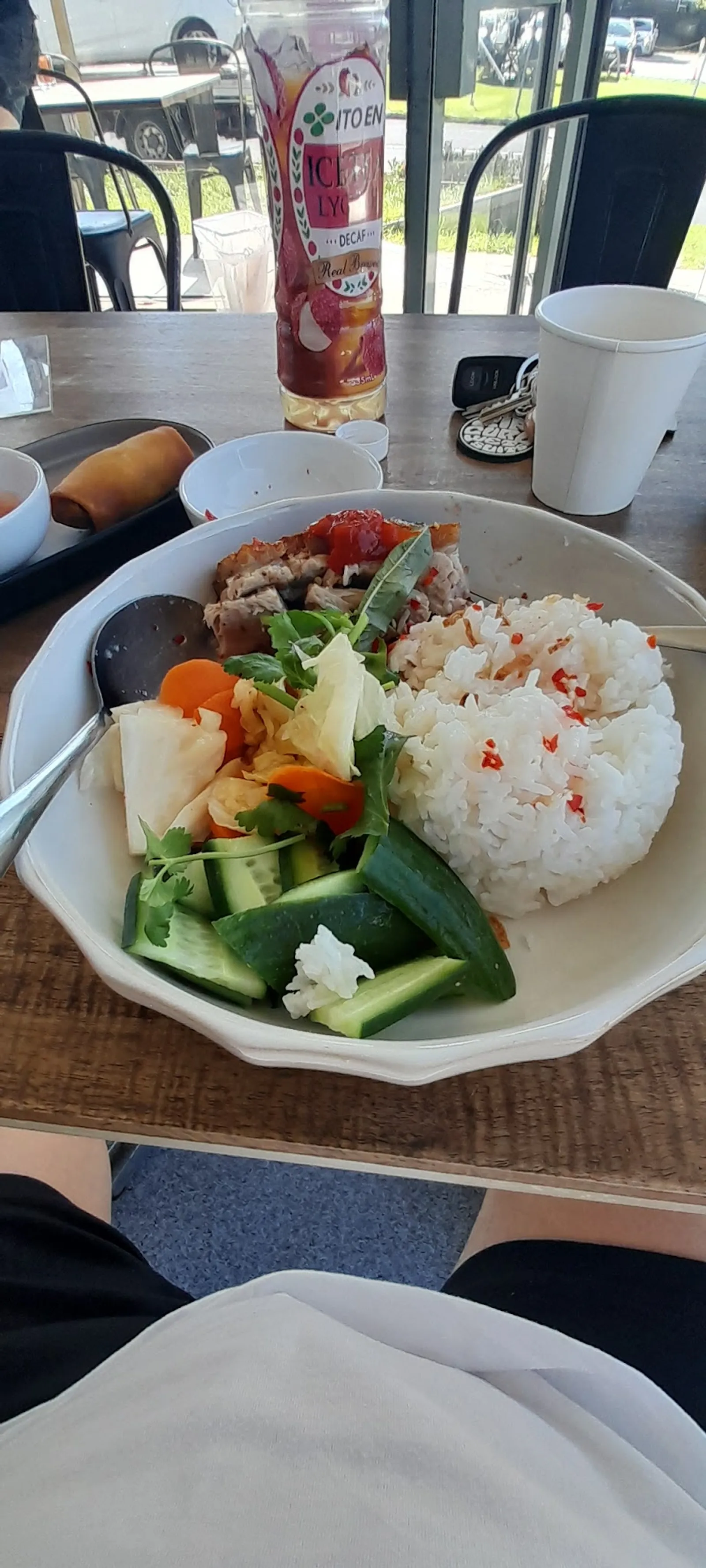 Bowl of chicken and rice with herbs and pickled veg on a table by the cafe window
