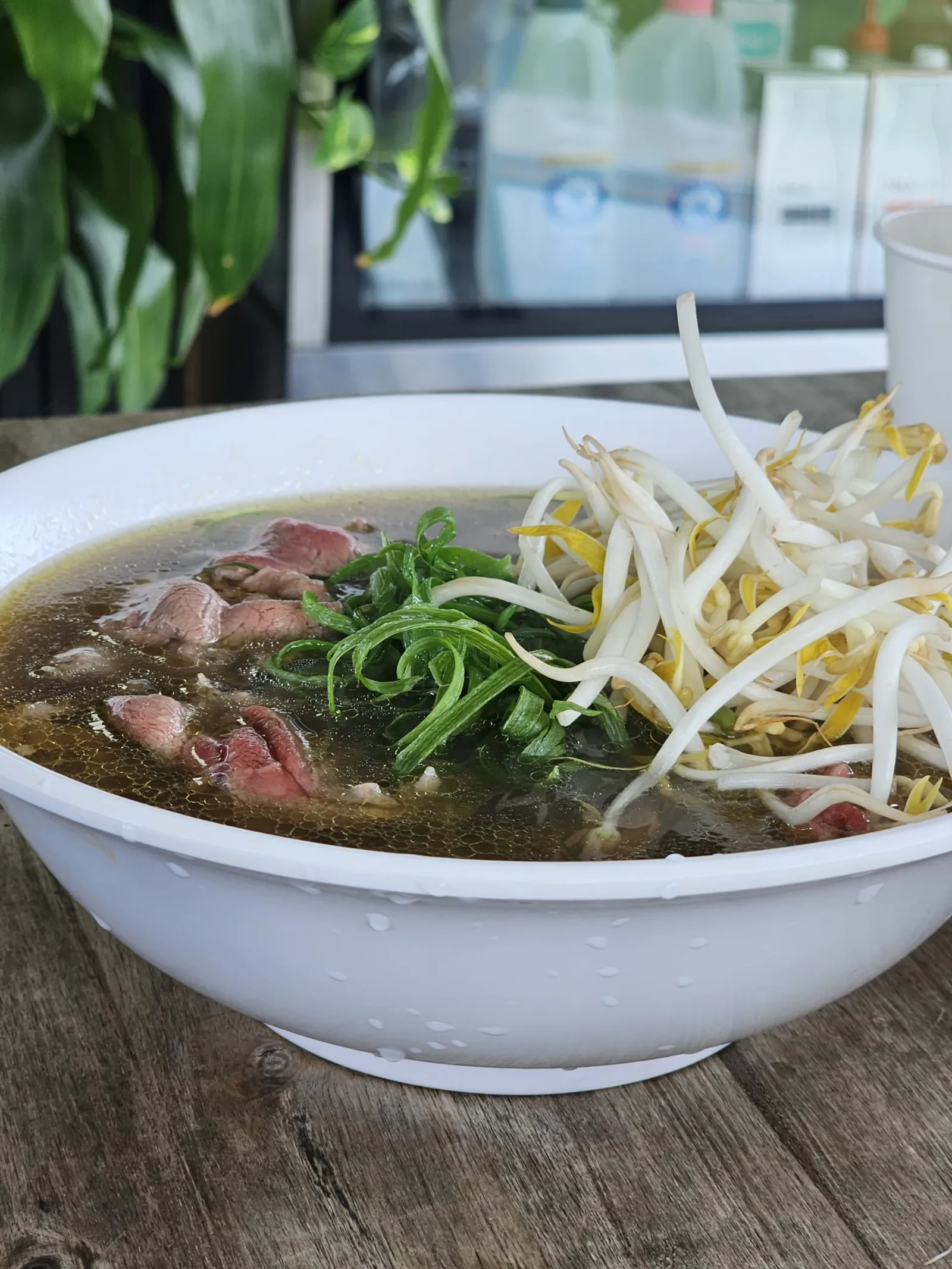 Bowl of beef pho with rare beef, spring onion and bean sprouts on a wood table